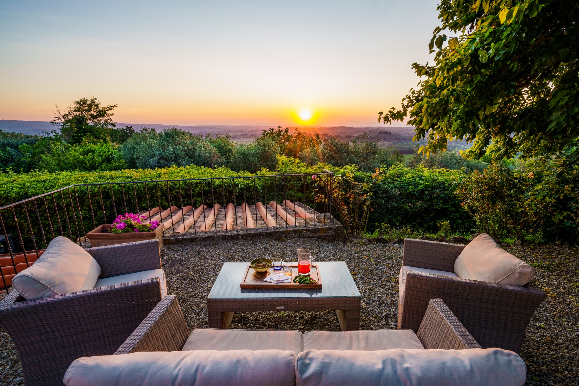 Outdoor terrace at Casa Pietraia in Certaldo with rattan sofas and a coffee table with drinks, overlooking the Tuscan hills at sunset