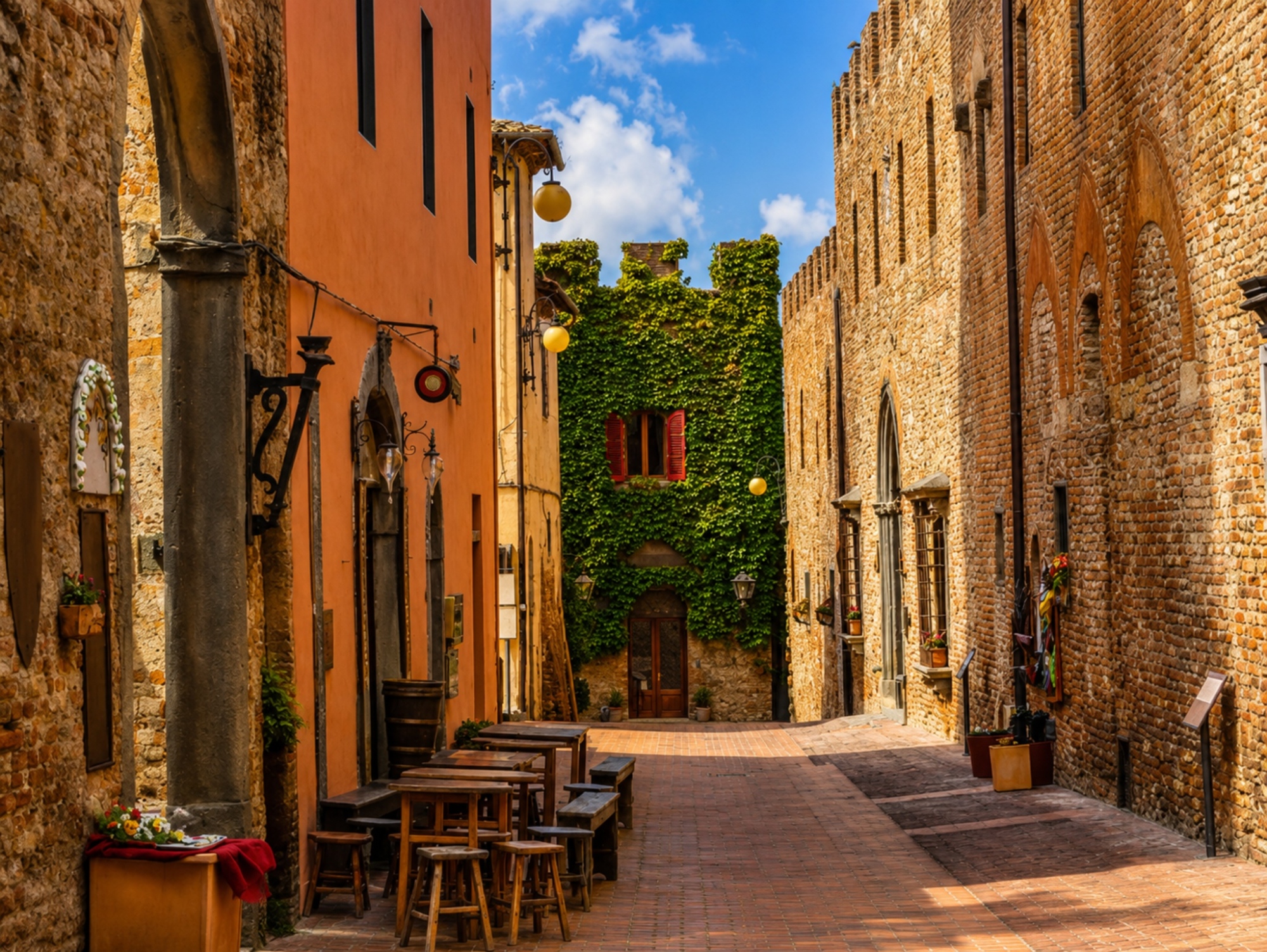 Medieval alley of Certaldo Alto with stone buildings, climbing ivy, and outdoor seating
