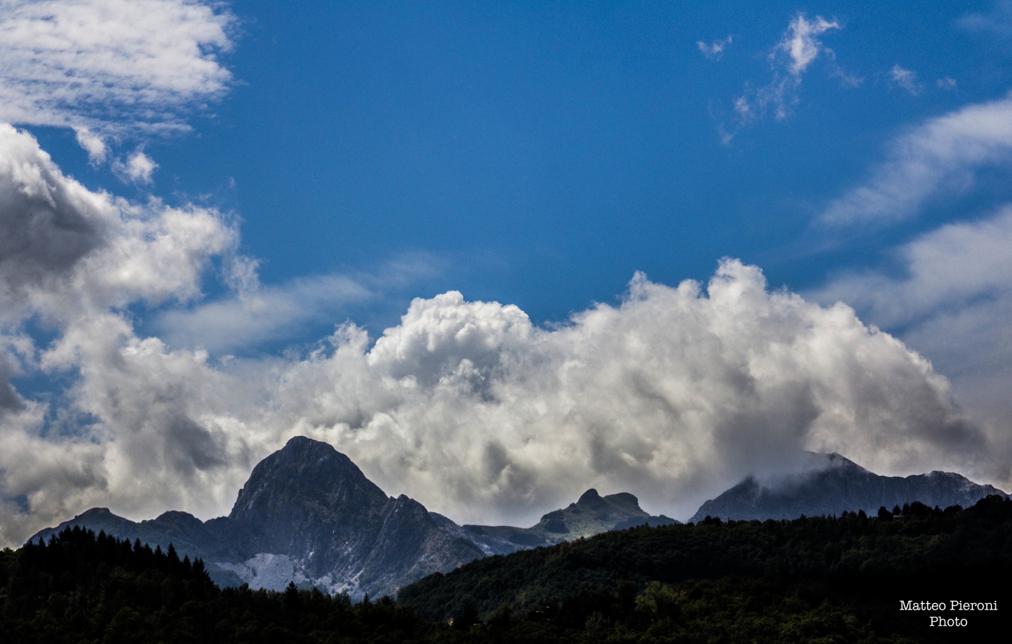 Panorama des Alpes apuanes avec les sommets de l’Omo Morto et du Pania, montagnes rocheuses se découpant sur le ciel, entourées de végétation et de vallées.