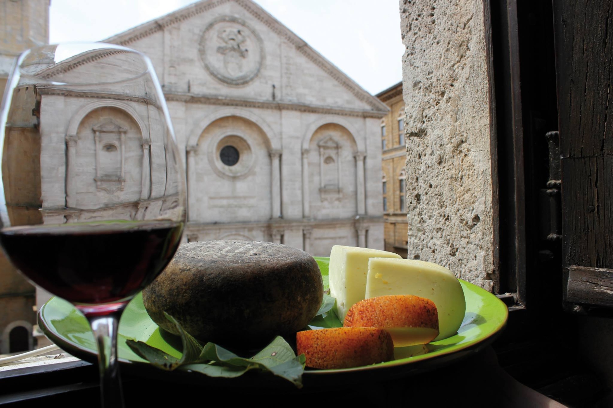 Vue depuis une fenêtre avec une assiette de pecorino frais assaisonné et un verre de vin au premier plan